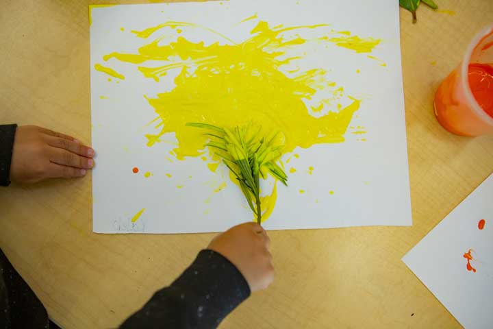 A child painting with leaves on a paper.