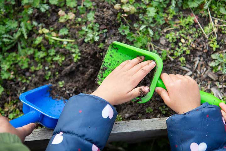 child's hands digging with a shovel in dirt