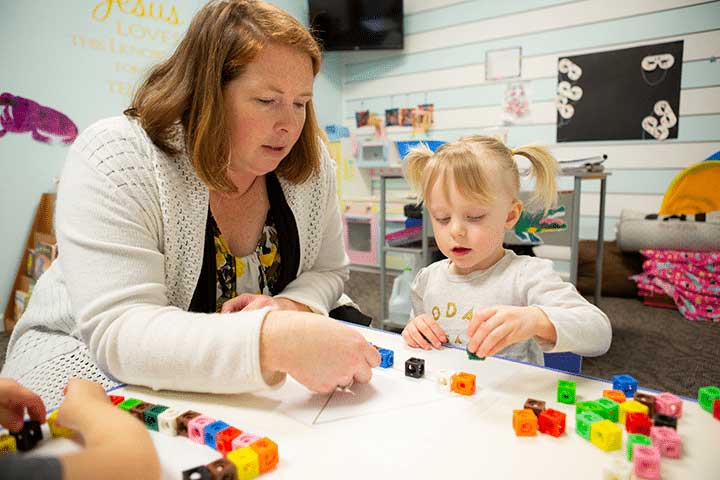 A teacher and preschooler building a triangle shape with cubes.