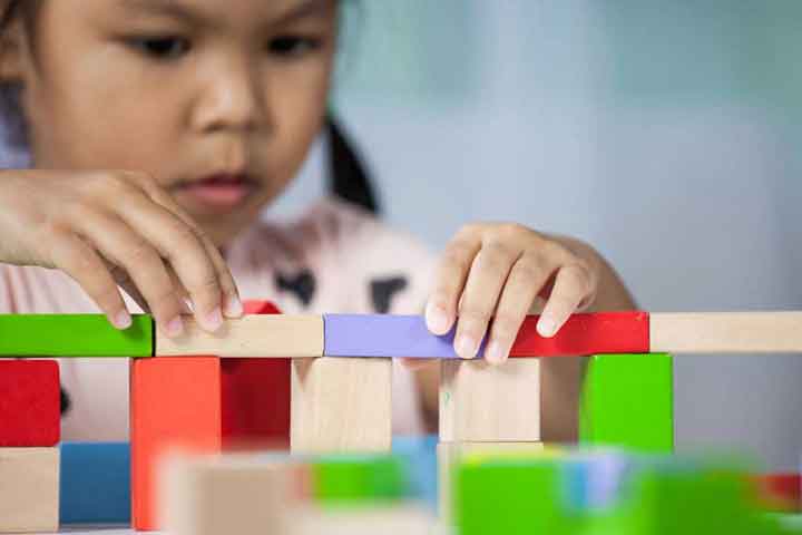 Focus on hands of cute little child girl playing with colorful wooden blocks in the room
